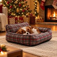 Grey and red plaid bolster pet bed with a sleeping Cavalier puppy by the Christmas tree and fireplace